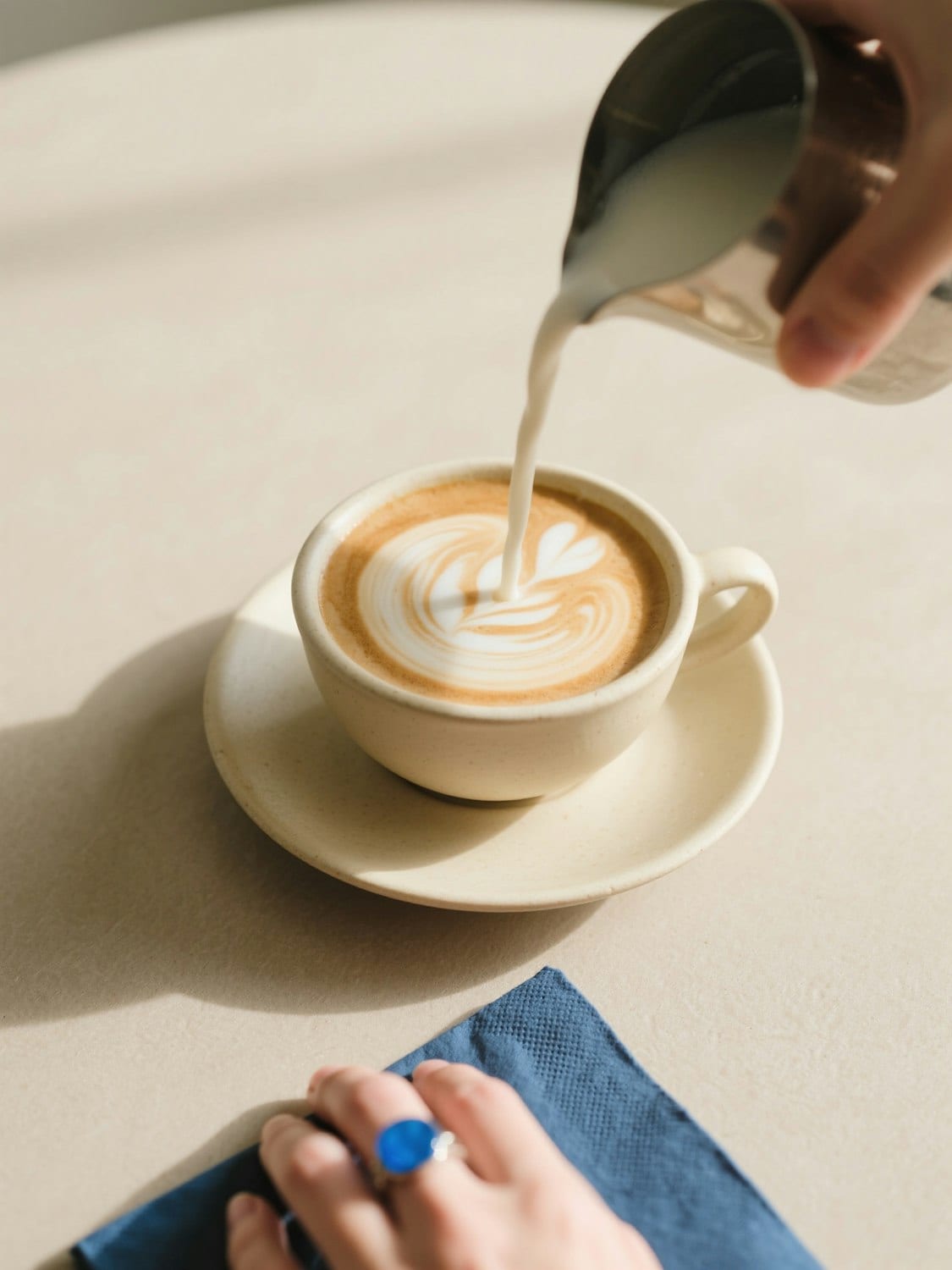 Krem rengi bir fincandaki kahveye süt dökülerek latte art yapılıyor